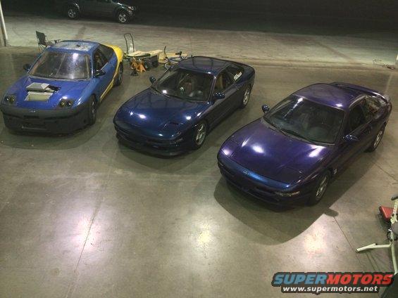 Three blue Ford Probe cars parked indoors, one with a yellow rear section and hood scoop