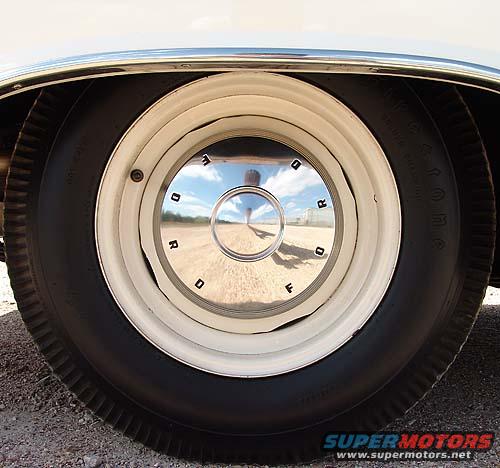 Chrome hubcap with 'FORD' lettering on a white rim, reflecting a cloudy sky and a person
