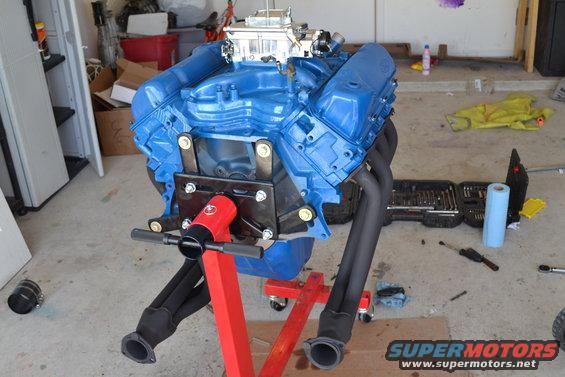 Blue V8 engine with black headers on a red engine stand
