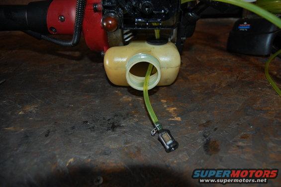 Close-up of a yellow fuel line and filter attached to a small engine's fuel tank