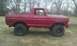 1978 Ford Bronco - A red pickup truck is parked on a grassy field with trees in the background.