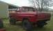 1978 Ford Bronco - A red 1978 Ford Bronco sits in a grassy yard next to a building, its top removed and suspension lifted.