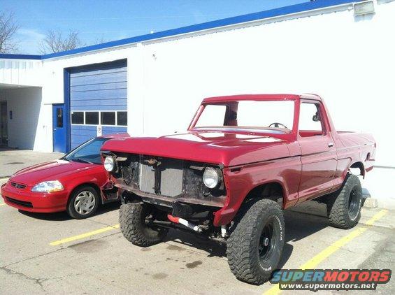 Red 1977 Ford F-150 pickup truck with missing grille, parked next to a red sedan