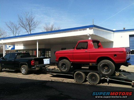 Red 1978 Ford Bronco on a trailer being towed by a black pickup truck