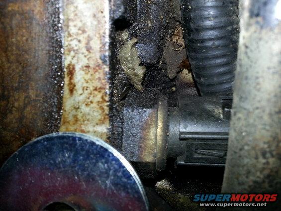 Close-up of a greasy engine part with a washer and electrical connector