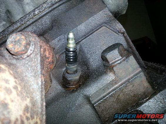 Spark plug in a greasy engine block, close-up view