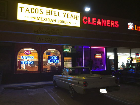 1964 Ford Ranchero parked at night in front of Tacos Hell Yeah! and Cleaners. Another car is parked to the right