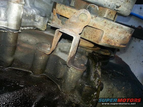 Close-up of rusty engine bracket on greasy transmission housing