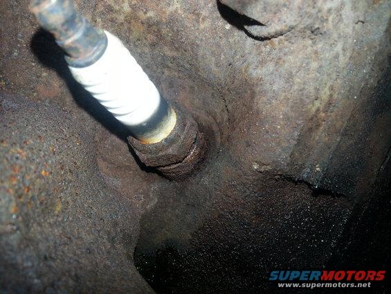 Spark plug screwed into a heavily rusted engine block with oil residue