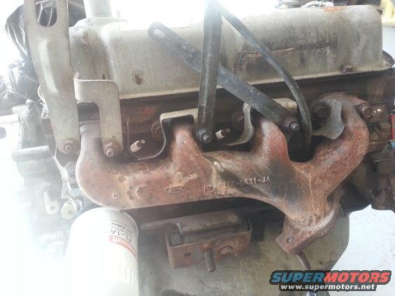 Close-up of a rusty Ford engine exhaust manifold with part number visible