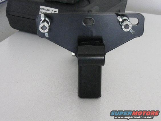Black metal hitch receiver part with bolts and nuts, resting on a white surface. Hitachi logo visible on a black case in background