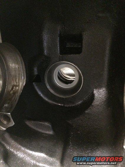 Black engine part with a circular opening and a bolt head visible