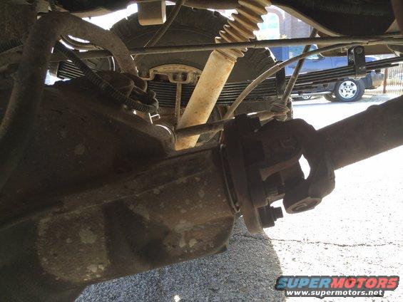 Close-up of driveshaft U-joint and rear suspension leaf springs. Another vehicle is visible in the background
