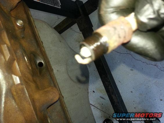 Spark plug held by gloved hand near rusty engine component