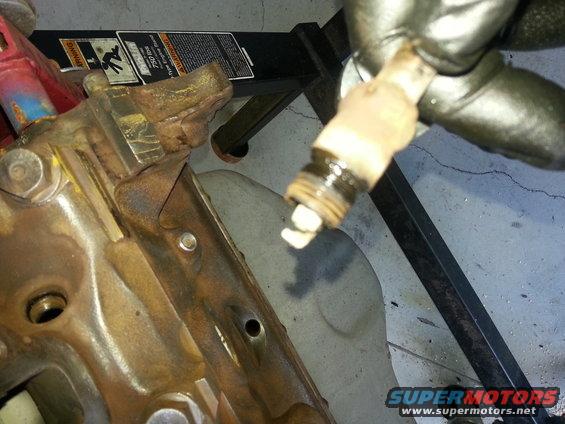 Spark plug removed from rusty engine block, Supermotors.net logo visible