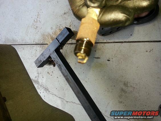 Spark plug held by gloved hand over metal tool on concrete floor