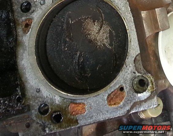Engine cylinder with piston visible, showing wear and carbon buildup