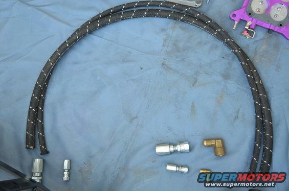 Braided fuel lines with assorted metal fittings laid out on a blue cloth surface