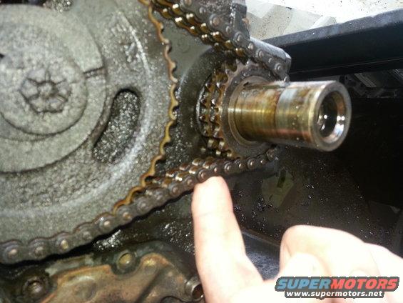 Close-up of engine timing chain and gears with a finger pointing