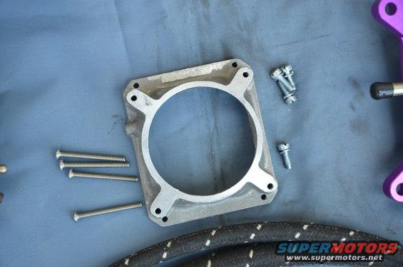 Carburetor spacer and assorted screws on a blue surface. Text reads SUPERMOTORS