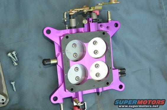 Purple aftermarket carburetor with four circular throttle plates and linkage. Several screws are visible on the left