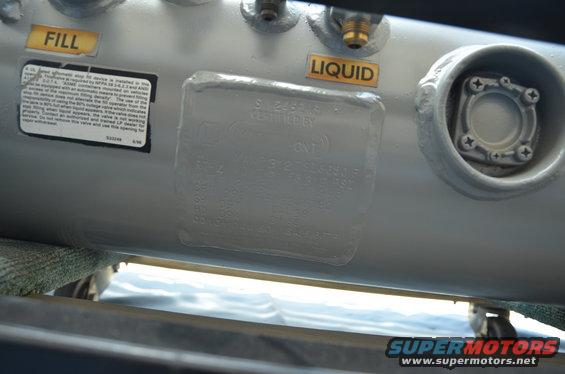 Silver propane tank with "FILL" and "LIQUID" labels and a certification plate