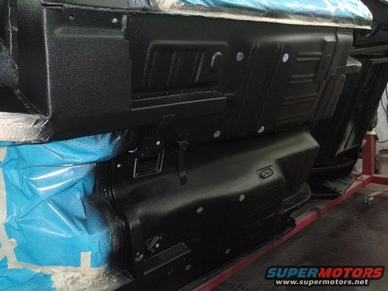 Underside of a black vehicle with protective blue masking tape, viewed from below