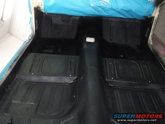 Car interior floor with black carpeting and raised sections for feet