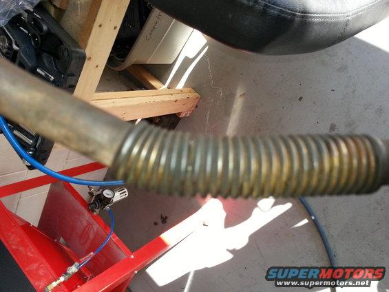 Corrugated metal pipe with blue hose and pressure gauge on red equipment