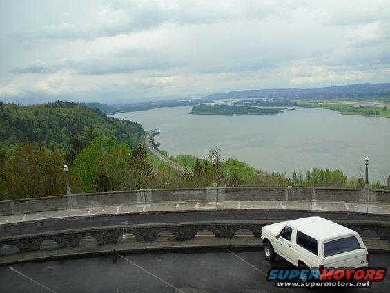 1990 Ford Bronco parked at a scenic overlook with a river and hills in the background