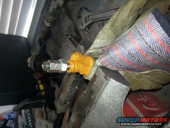Close-up of a yellow automotive fitting with metal nuts attached, held in a vise
