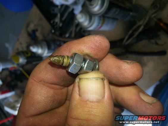 Hand holding a metal part with two nuts and a brass tip