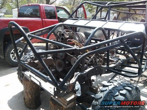 Off-road buggy frame on blocks, engine visible. Red pickup truck in background