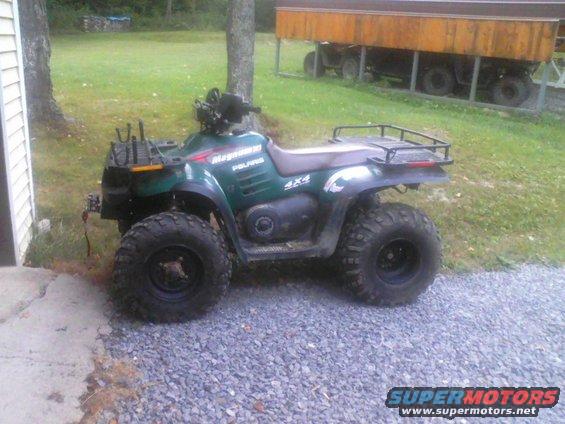 Green Polaris Magnum 4x4 ATV parked on gravel next to a building