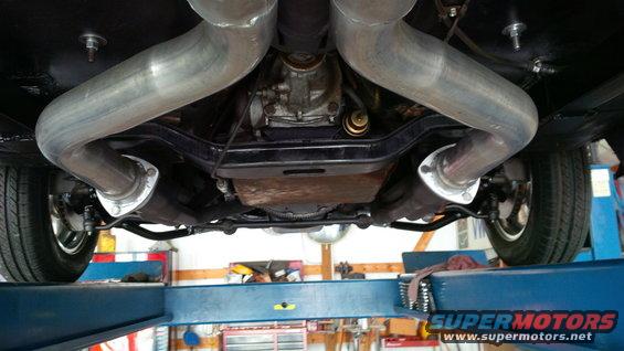 Underside view of a car's dual exhaust system and differential, raised on a lift