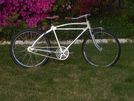 Chrome frame bicycle with leather seat and handlebars, parked on grass in front of pink flowers