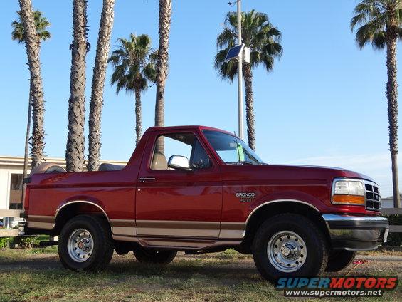 Red 1994 Ford Bronco with tan trim, parked on grass under palm trees