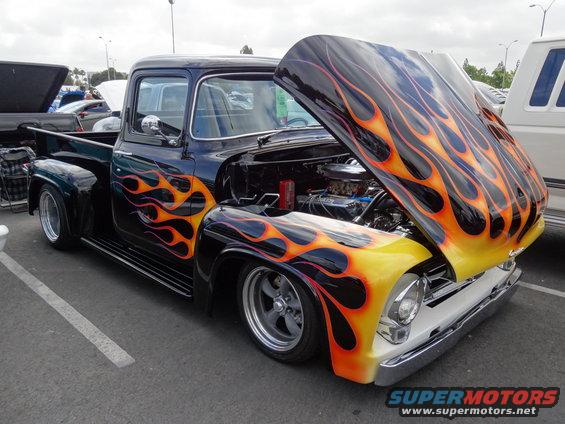 Black 1956 Ford F-100 pickup truck with custom flame paint and lowered suspension, hood open showing engine