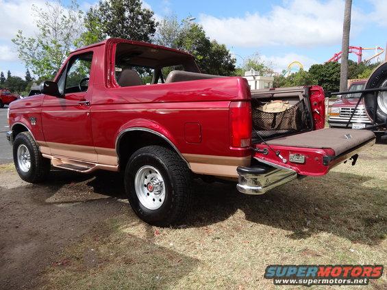 Red 1994 Ford Bronco with tailgate down, showing cargo area and spare tire carrier on another vehicle behind it