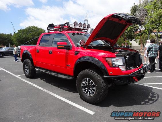 Red pickup truck with hood open, roof rack, and off-road tires