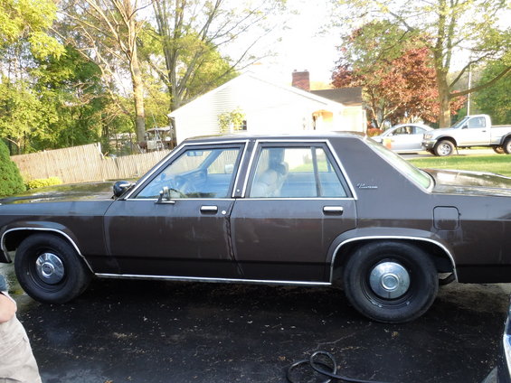Brown Ford sedan parked on wet asphalt, with a silver pickup truck and car in the background