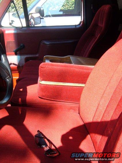 Red velour interior with sunglasses on the floor, showing a portion of the dashboard and a side mirror reflection