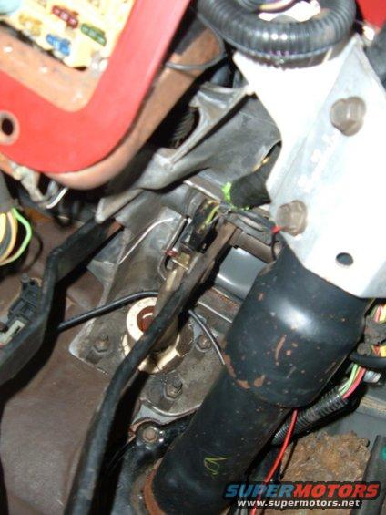 Close-up of vehicle interior showing steering column, wiring harnesses, and fuse box