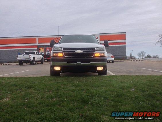 Front view of a white pickup truck parked in front of a building. Another white pickup is visible to the left