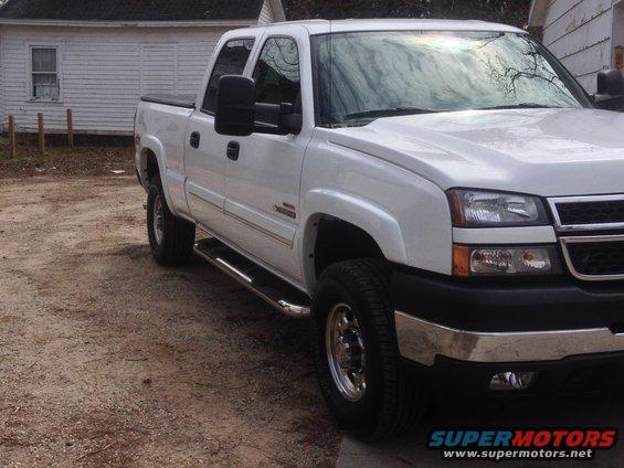 White pickup truck with chrome side steps and tow mirrors, parked on a dirt lot
