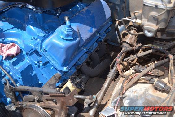 Close-up of a blue Ford V8 engine with exhaust manifolds and wiring. A pink rag is on the engine block