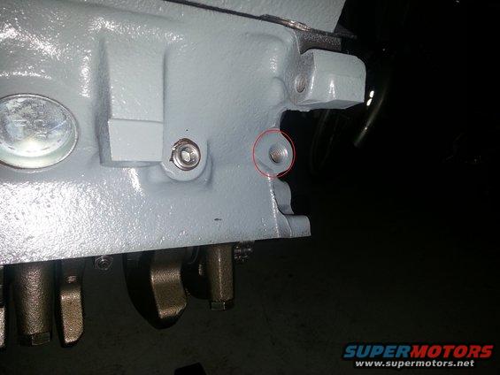 Close-up of a gray engine block with visible bolts and a threaded hole circled in red