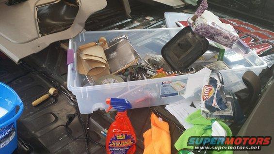Interior of a vehicle's cargo area with a clear storage bin filled with tools, cleaning supplies, and snacks