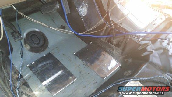Vehicle interior floor showing soundproofing material and exposed wiring. Includes pedals and a rubber grommet