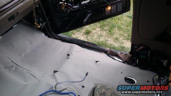 Car interior with soundproofing material laid on the floor and door panel removed, showing wiring